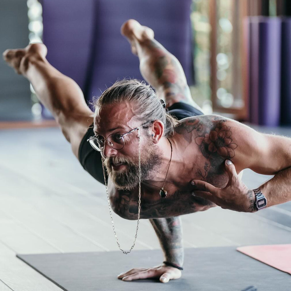 Man performing a yoga pose on a mat with a phone and camera equipment nearby.